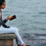 A young woman enjoys a peaceful moment by the sea, engrossed in her smartphone at Diu, India.