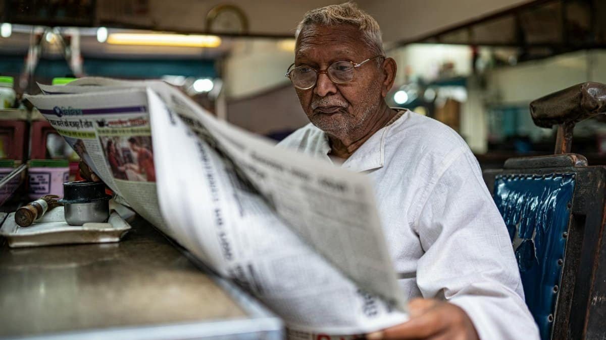Elderly man reads a Hindi newspaper in a local Varanasi shop, capturing daily life.