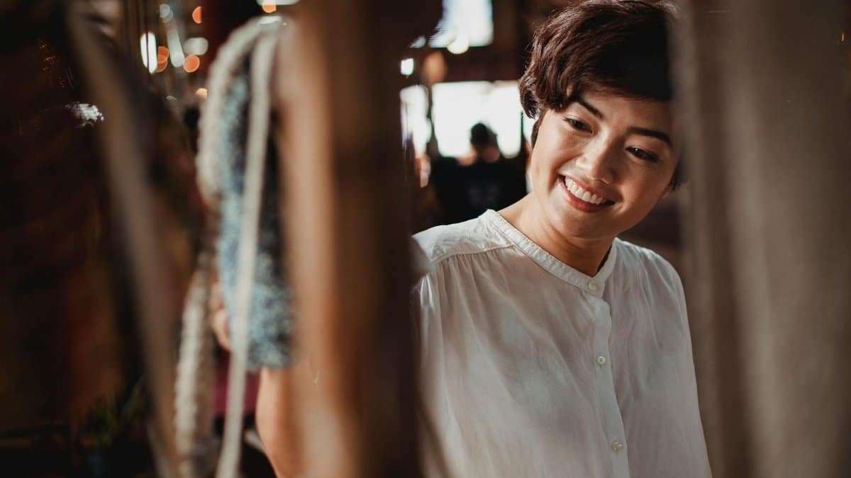 Happy woman browsing items at an outdoor local market, enjoying a sunny day.