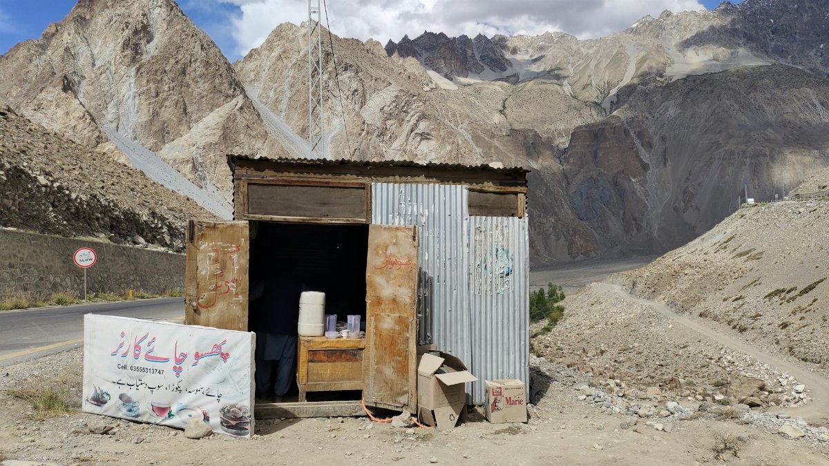 Small roadside shack offering drinks against a stunning mountainous backdrop.