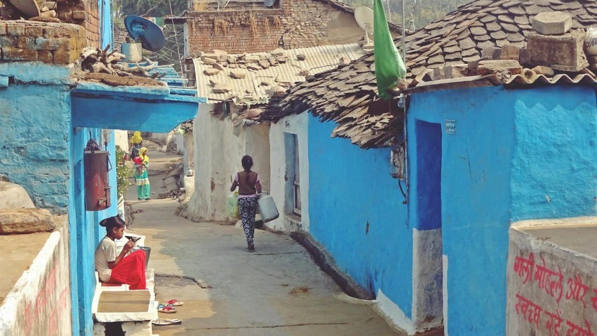 A vibrant village street scene featuring blue-painted houses and local residents going about their daily activities.