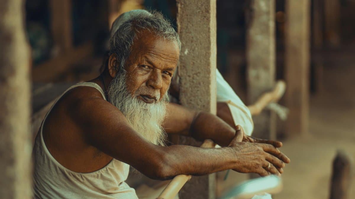 Portrait of an elderly man in Dhaka, Bangladesh, sitting thoughtfully outdoors.