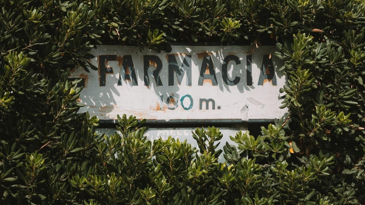 A vintage "Farmacia" sign surrounded by lush green leaves in Benidorm, Spain.