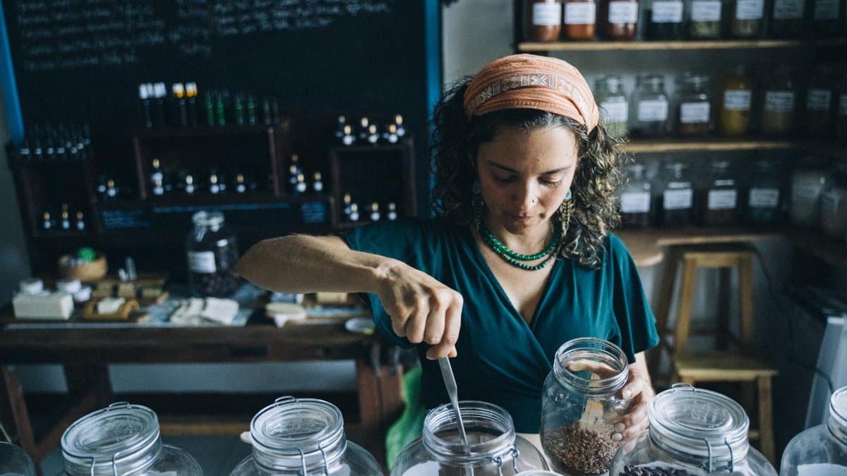 Woman in eco-friendly store preparing organic products using glass jars with a variety of ingredients.