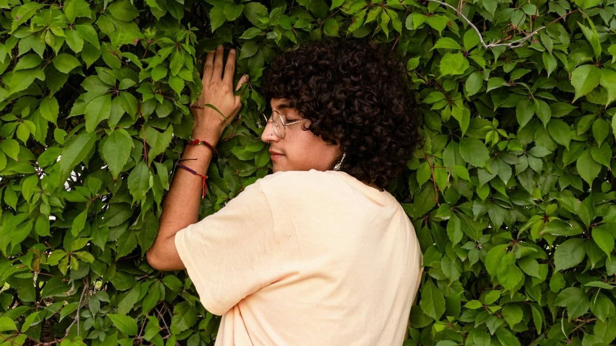 Individual enjoying nature by embracing a green leafy wall, symbolizing tranquility and connection with nature.