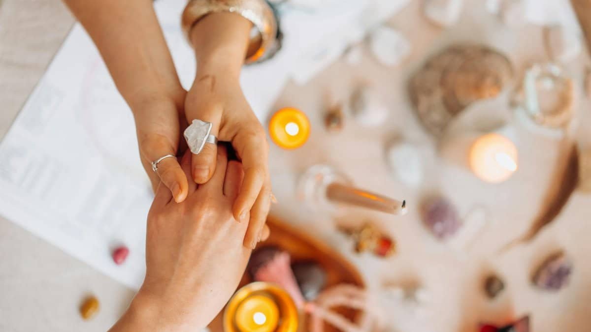 Hands exchanging energy with crystals and candles on a mystic table setting.