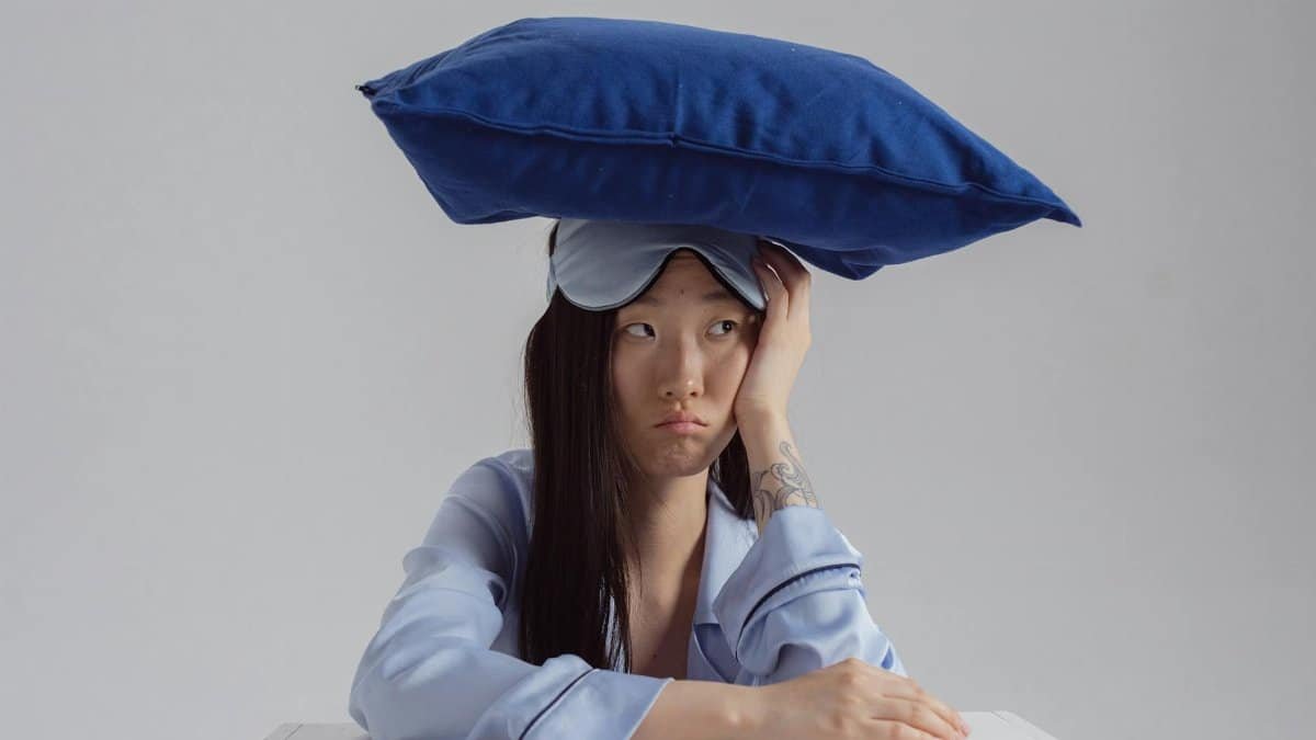 Tattooed woman with pillow and sleep mask showing insomnia concept.