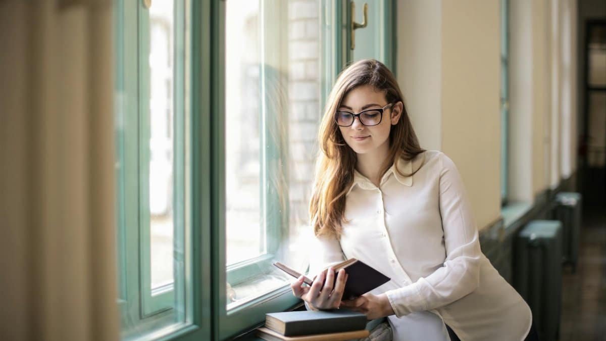 Woman in white long sleeves reading by the window in a peaceful indoor setting.