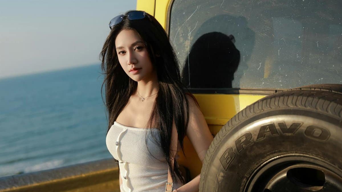 Woman by a jeep at the beach, enjoying a sunny day by the ocean. Fashionable and casual outdoor lifestyle scene.