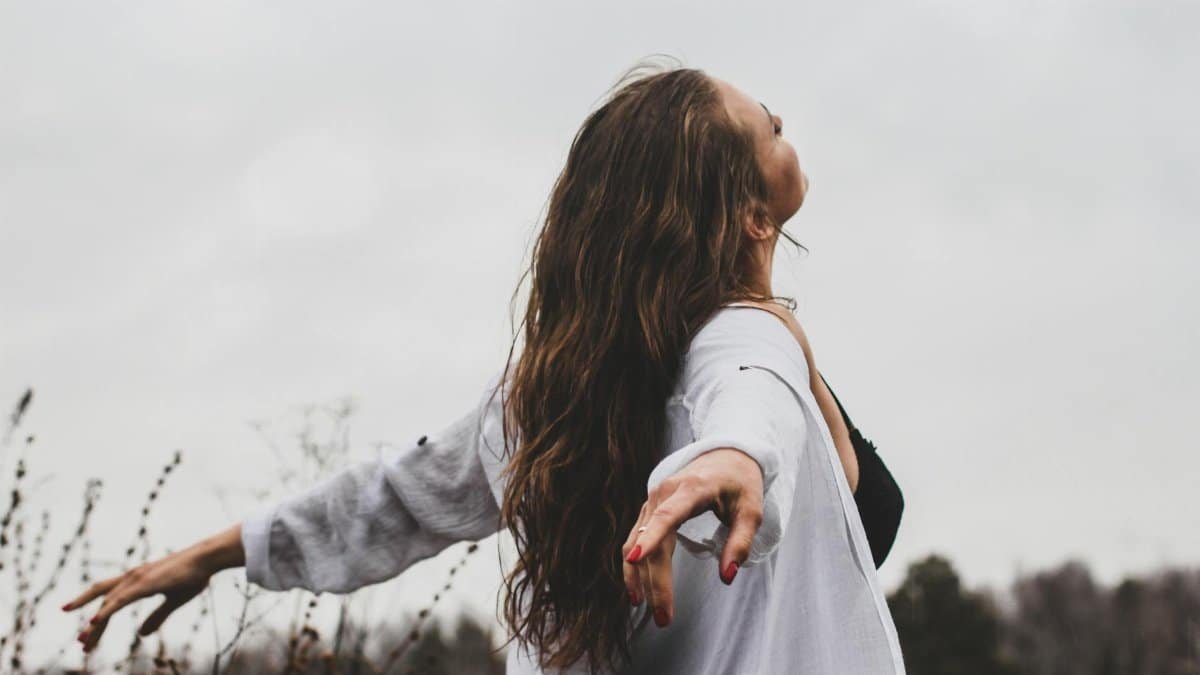 A woman with long hair joyfully embracing nature in an open field.