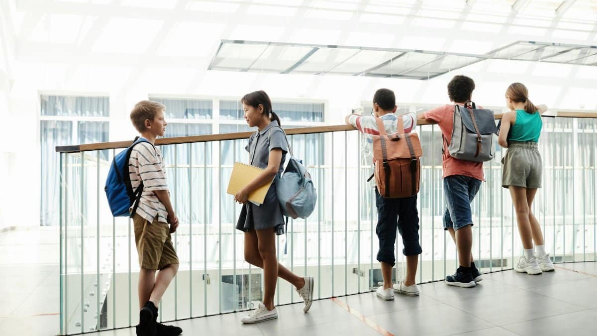 A group of diverse students chatting in a bright school hallway, carrying backpacks.