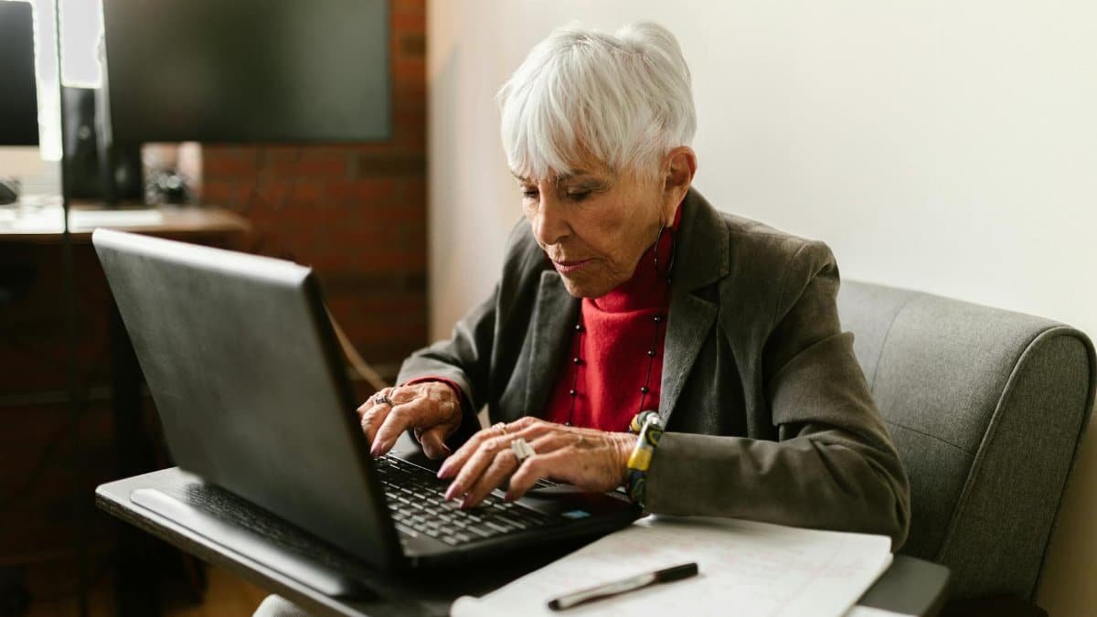 Senior woman with gray hair working on a laptop in a cozy home office setting.