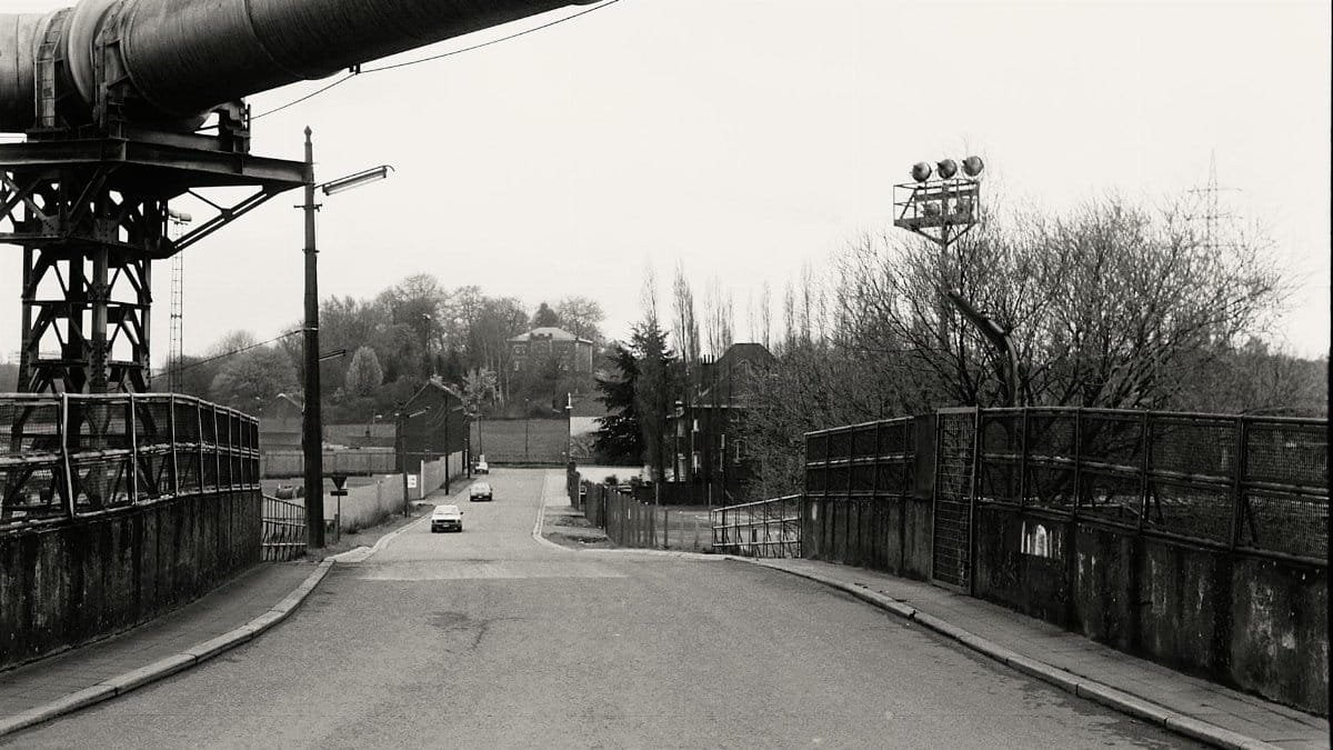 Black and white photo of rural road with industrial pipeline and bridge.