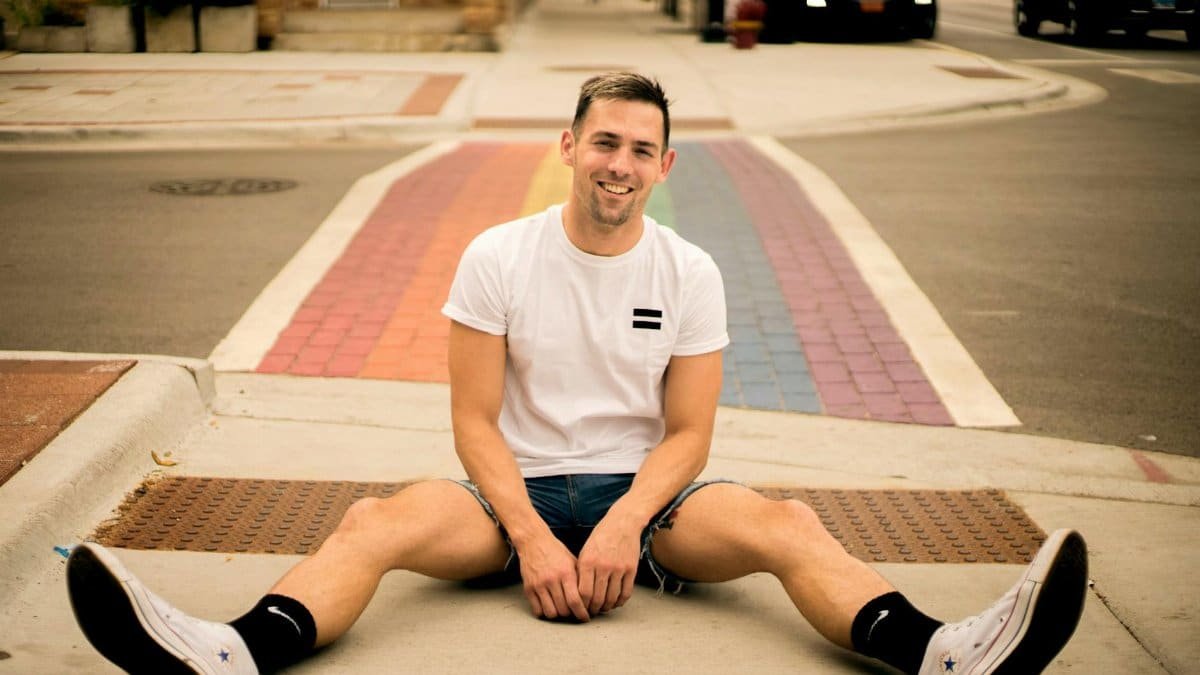 Happy young man sitting on a rainbow crosswalk in Chicago, smiling at the camera.