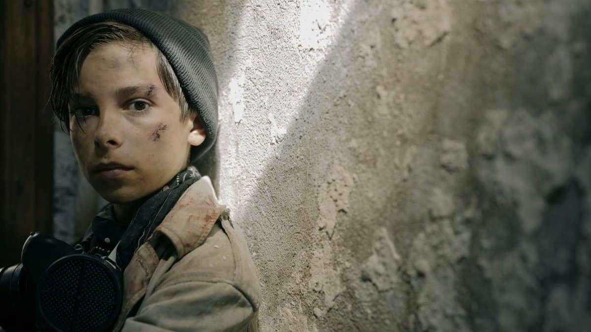 A young boy in a post-apocalyptic setting looking determined, wearing survival gear.