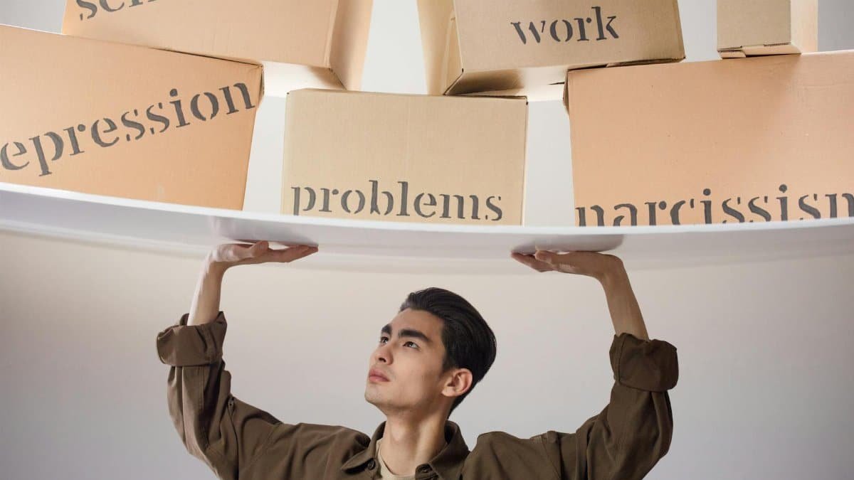 Young man struggles with metaphorical burdens symbolized by labeled boxes suspended above him.