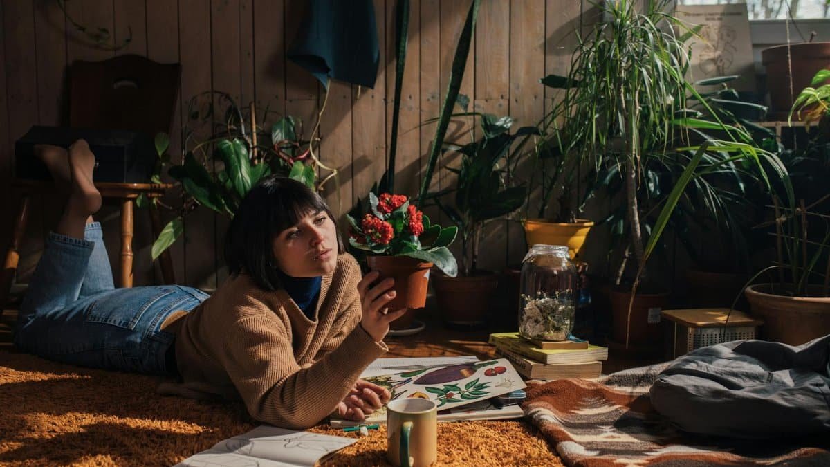 Woman relaxing indoors with plants, wearing sweater and denim. Home warmth.