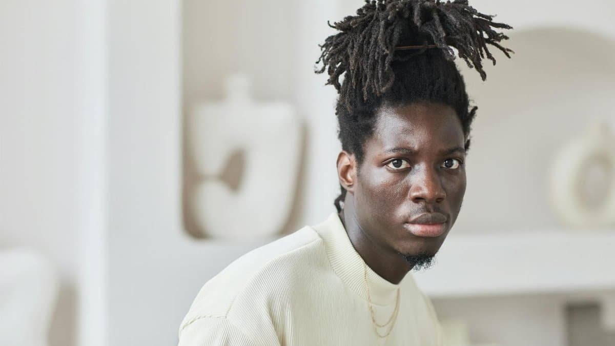 Close-up portrait of a fashionable man with dreadlocks looking intense indoors.