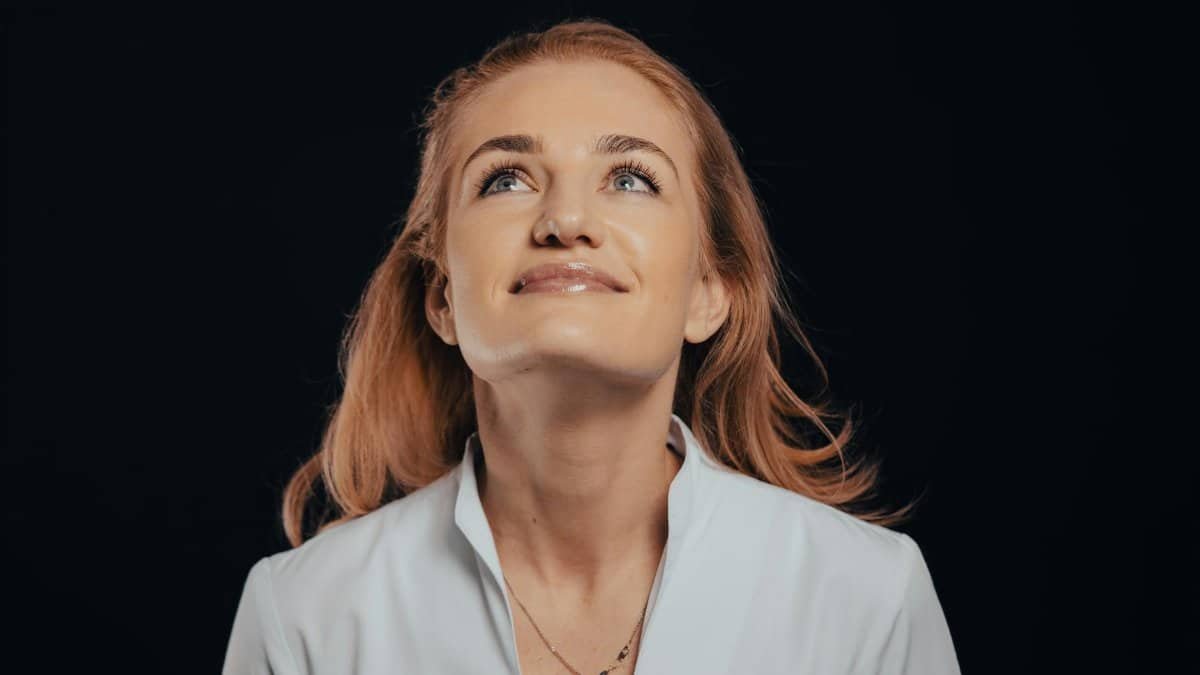 A joyful woman with blonde hair gazes upwards against a dark background, embodying optimism and confidence.