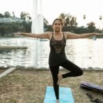 A woman performs yoga in a serene park beside a lake, promoting relaxation and mental wellness.