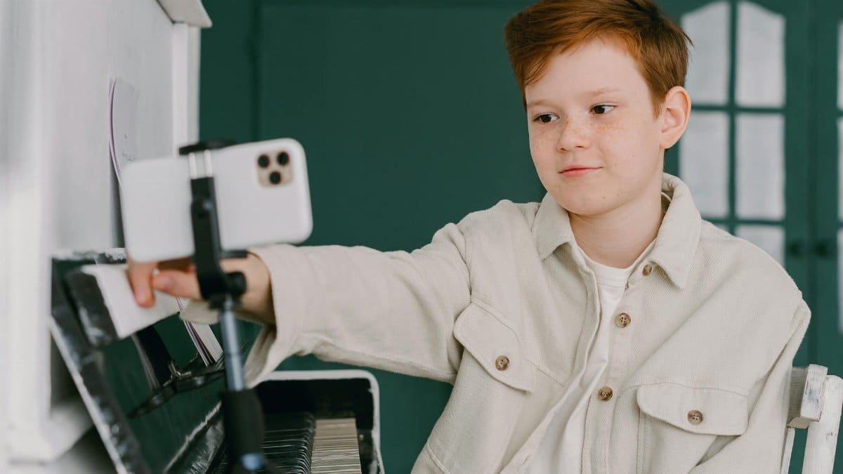 A young boy records a video using a smartphone at a piano, showcasing modern technology use.