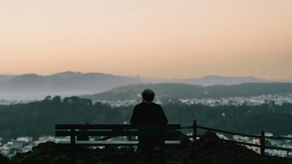 A man sits on a bench overlooking San Francisco at sunset, capturing a serene and contemplative moment.