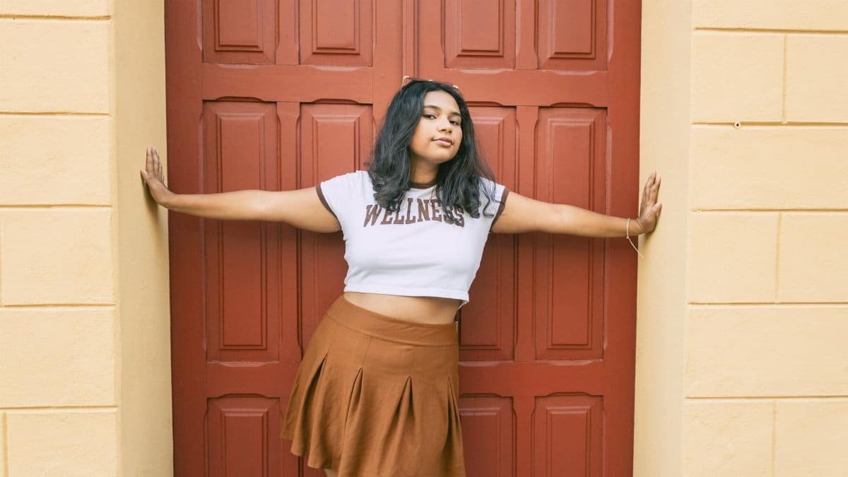 Stylish young woman in a wellness t-shirt poses confidently against a red door in an urban setting.