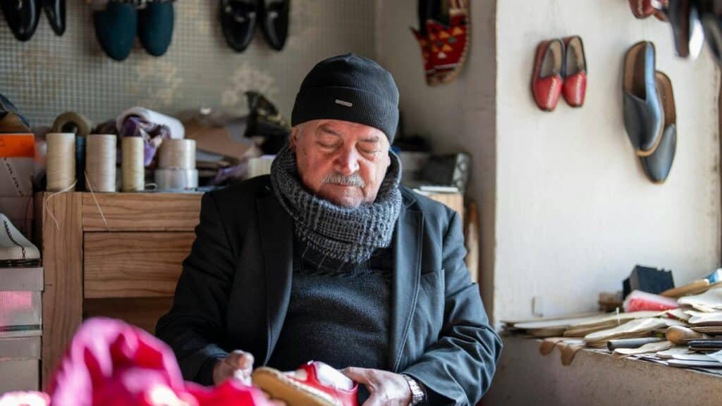 An elderly shoemaker in Kahramanmaraş, Türkiye, crafting shoes in his workshop surrounded by materials.