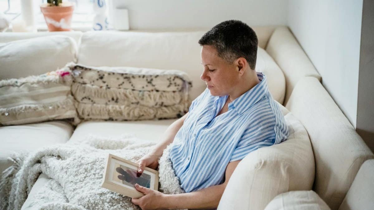 A woman with short hair sits on a cozy sofa holding a picture frame. Calm and reflective mood.