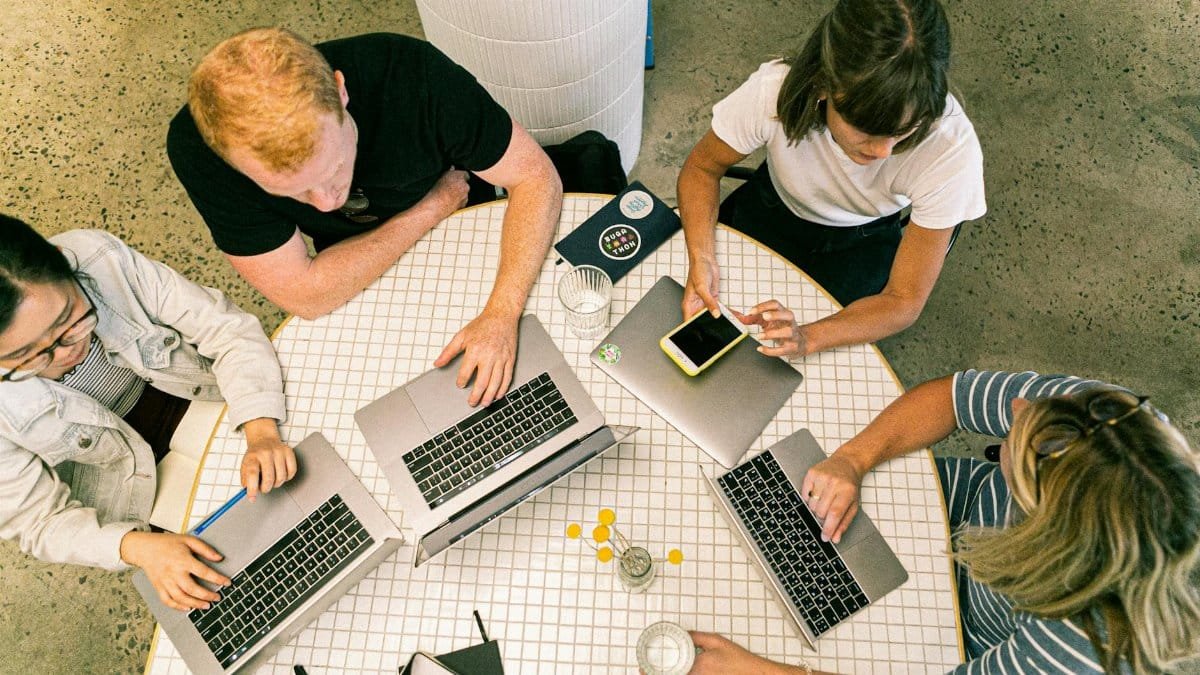 Top view of team collaborating in a modern office around laptops, discussing ideas.