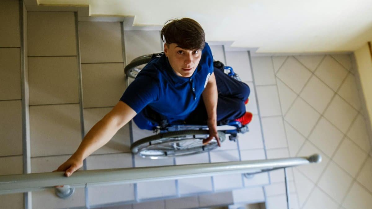 High angle view of person in wheelchair navigating stairs indoors, highlighting accessibility challenges.