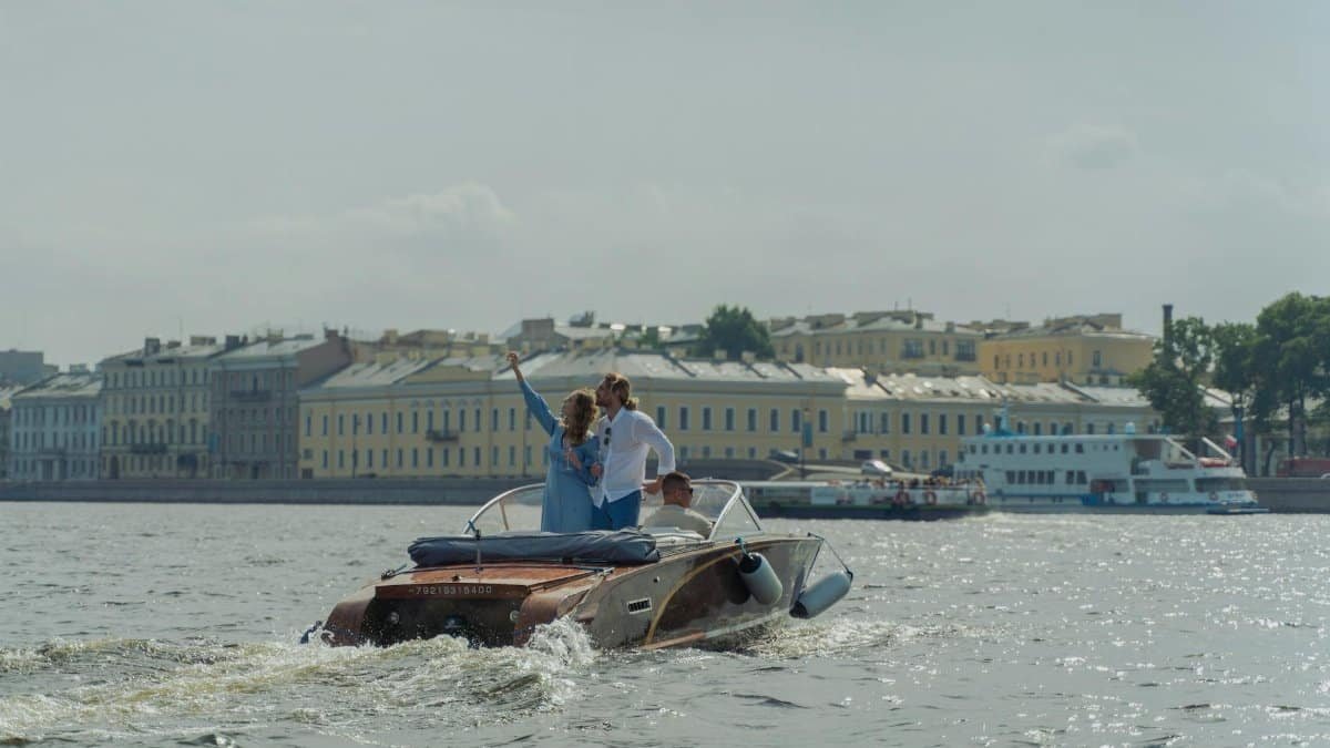 A couple enjoys a romantic boat cruise on a sunny day alongside historic urban architecture.