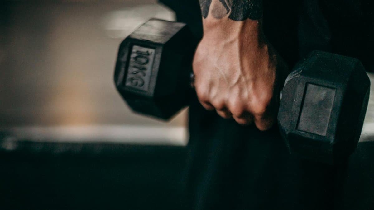 Close-up of a tattooed arm holding a 10kg dumbbell during a workout session indoors.