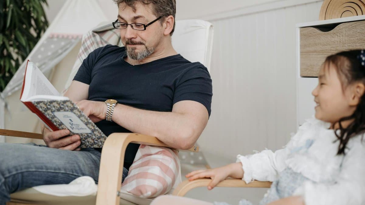 A father and daughter share a bonding moment reading a book indoors.