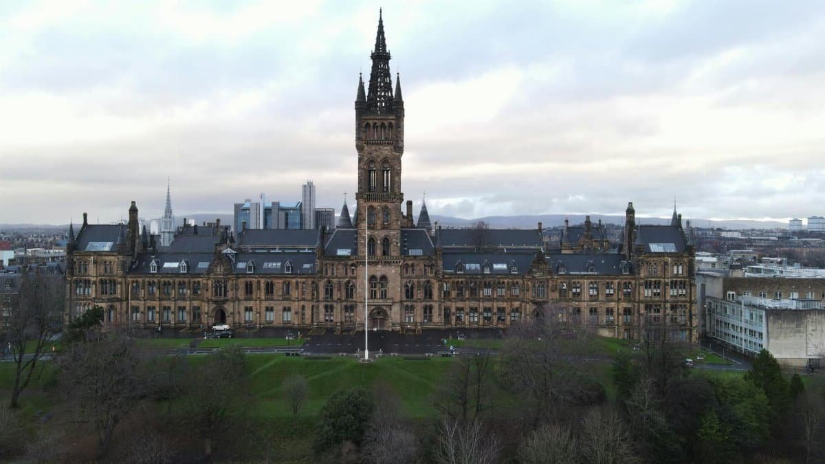 Aerial view of the historic University of Glasgow building surrounded by green trees under a cloudy sky.