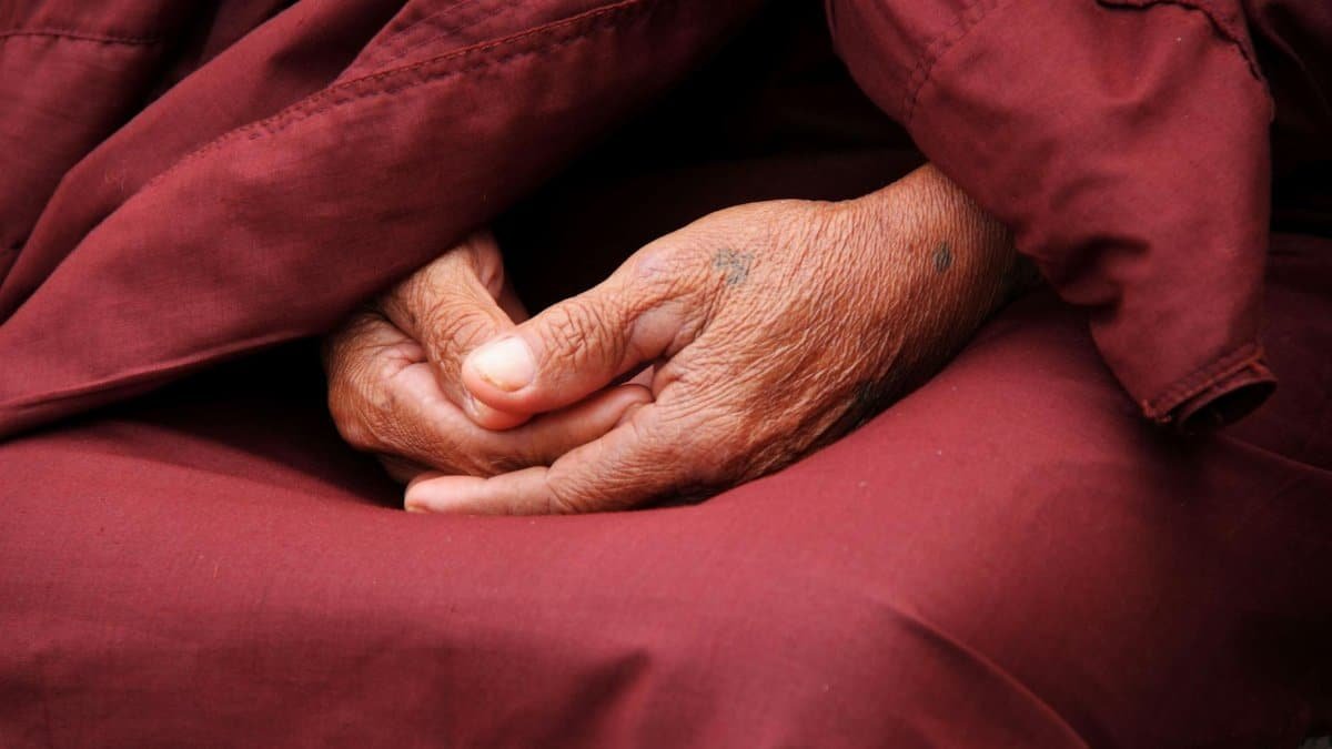 Close-up of a monk's hands in prayer, wrapped in maroon robe, symbolizing peace and spirituality.