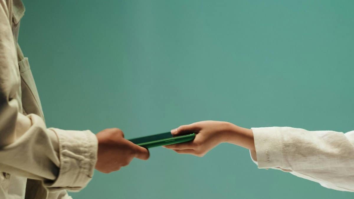 Two people exchanging a green mobile phone against a solid green background.