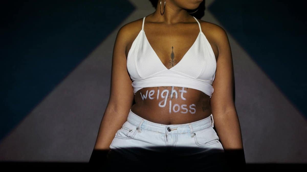 Confident woman showing weight loss message painted on her stomach, symbolizing motivation and lifestyle change.