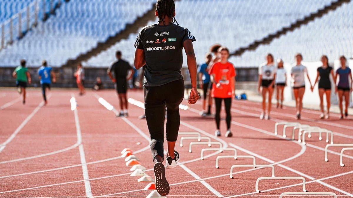 An athlete performing drills on an outdoor track in Lisbon with hurdles and cones.