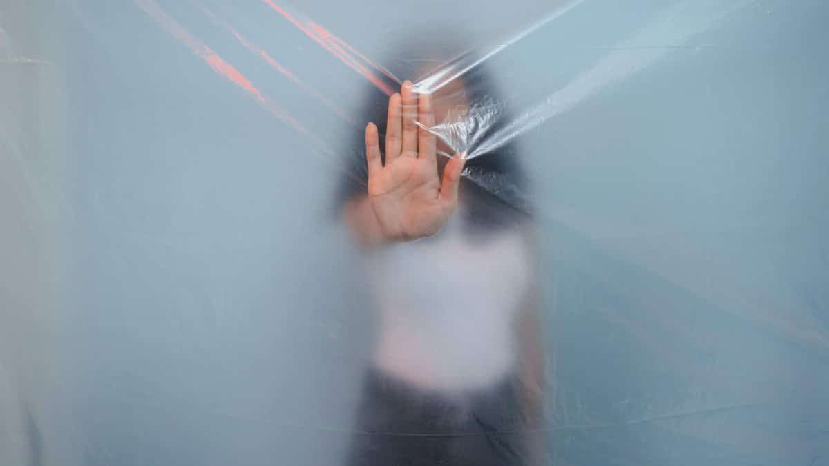 Blurred image of a woman pressing her hand against a translucent plastic sheet, creating a surreal effect.