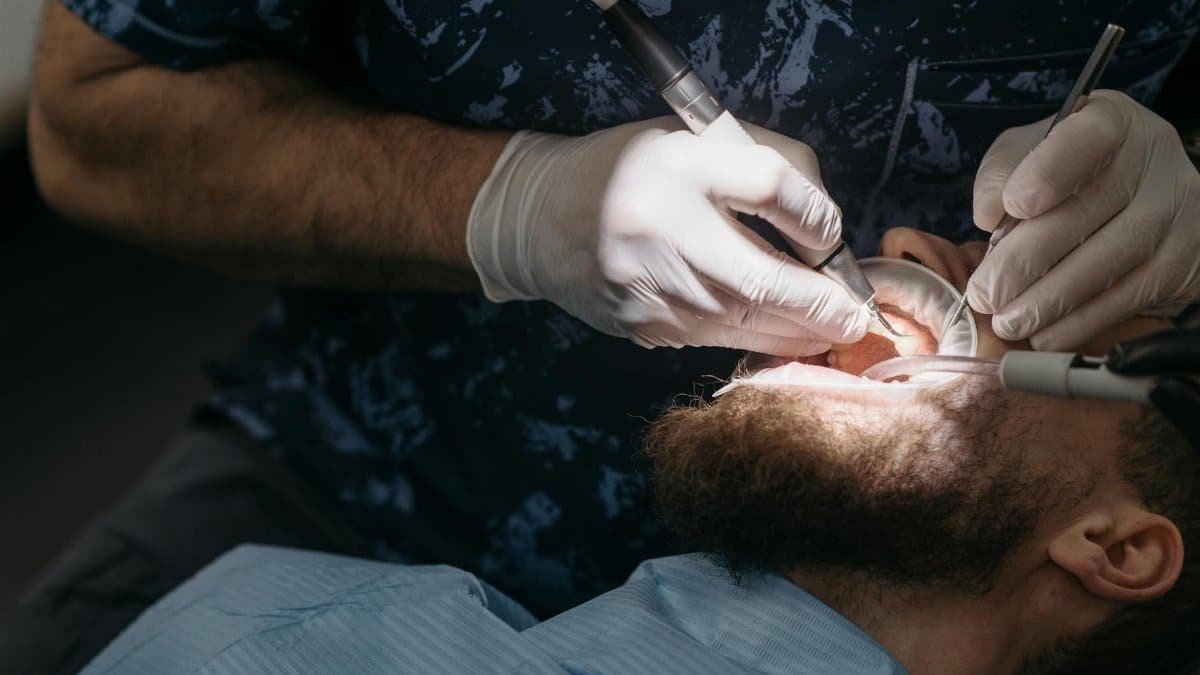 Dentist using tools for dental examination on a bearded male patient.