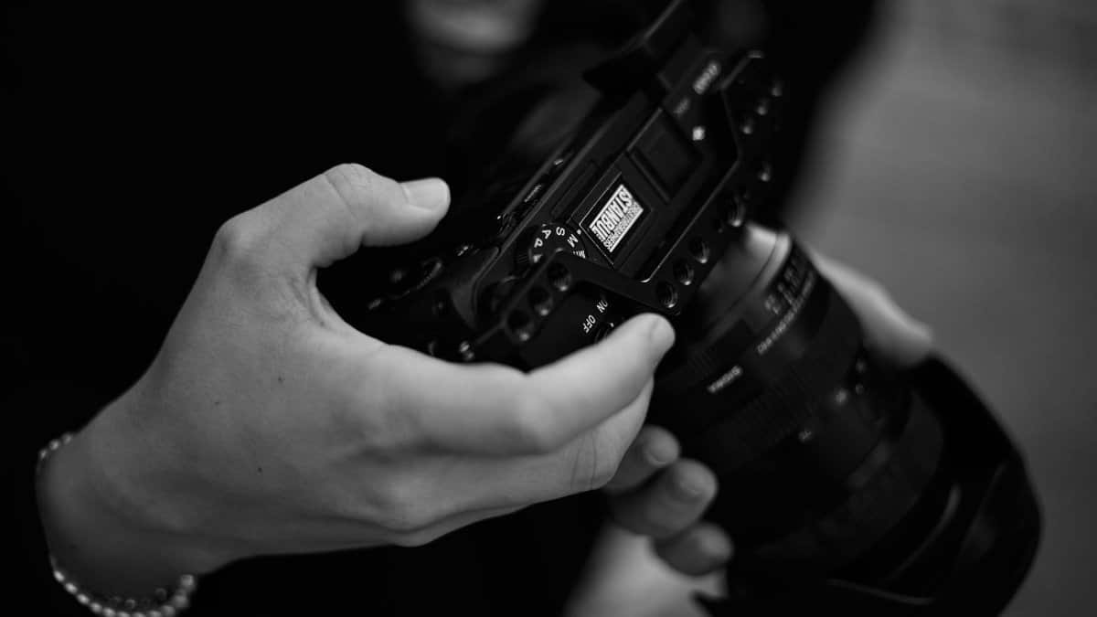 Professional photographer's hands grip a DSLR camera, showcasing precision and focus in black and white.
