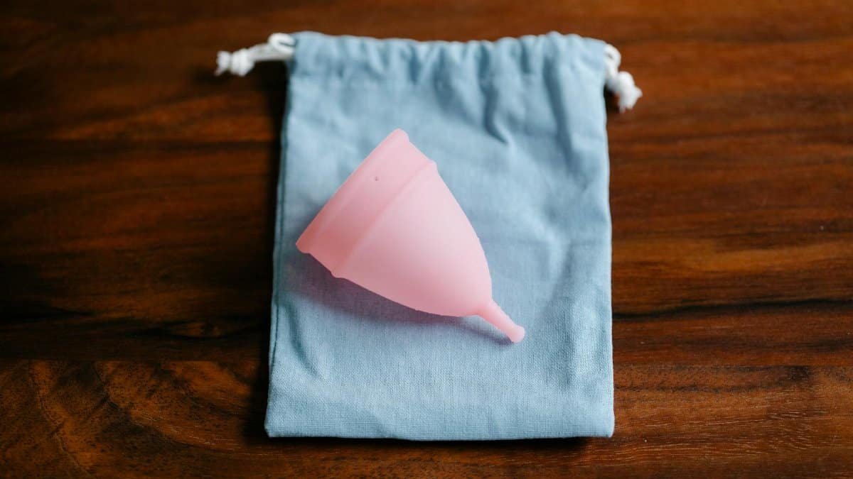 Top view of pink menstrual cup for feminine hygienic procedure on cloth bag placed on wooden table in light room