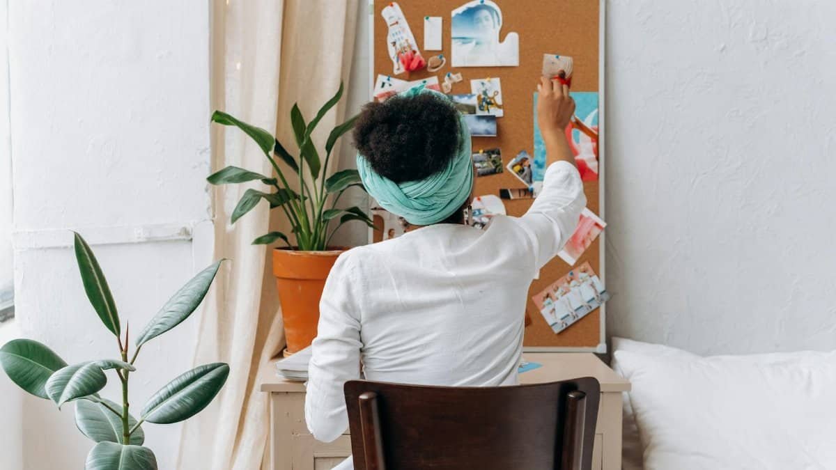 A woman in a cozy room organizing a vision board with photos and ideas.