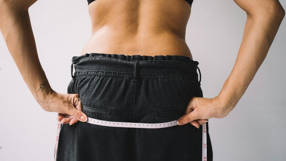A person measuring their waist with a tape measure, symbolizing fitness goals.