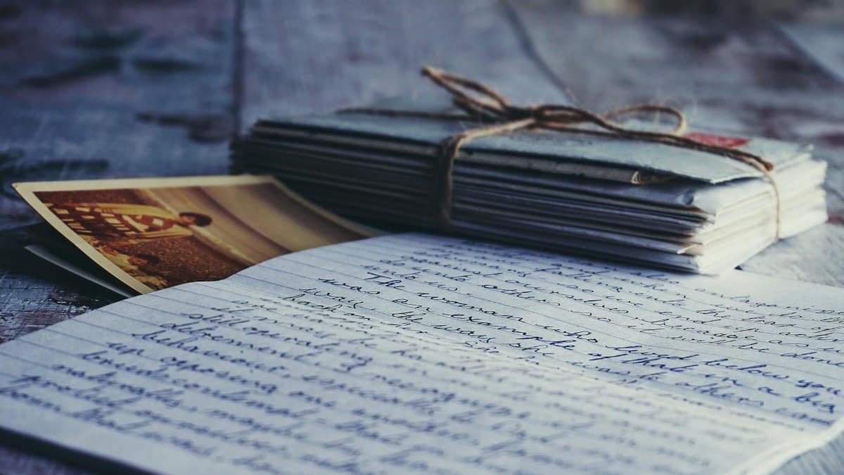Stack of vintage letters and photographs tied with string on a rustic wooden table.