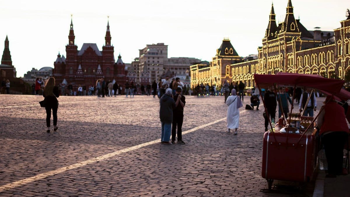 A bustling city square at dusk, illuminated buildings and people create a vibrant urban atmosphere.