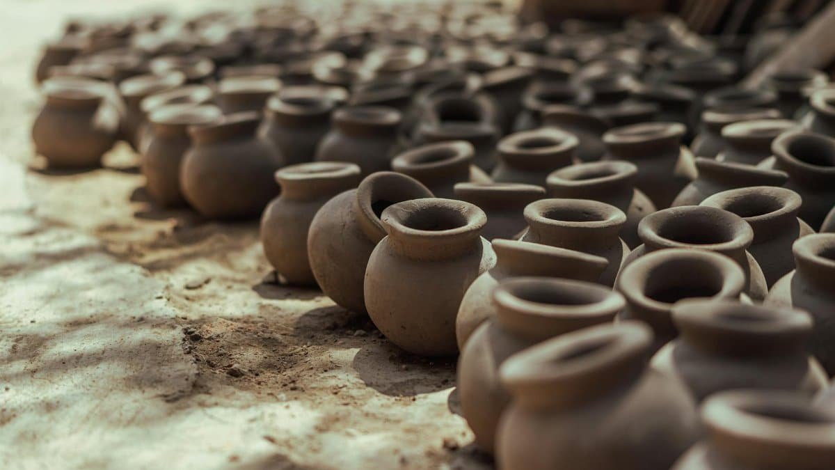 Rows of handmade clay pots drying on the ground under the sun, showcasing traditional pottery techniques.