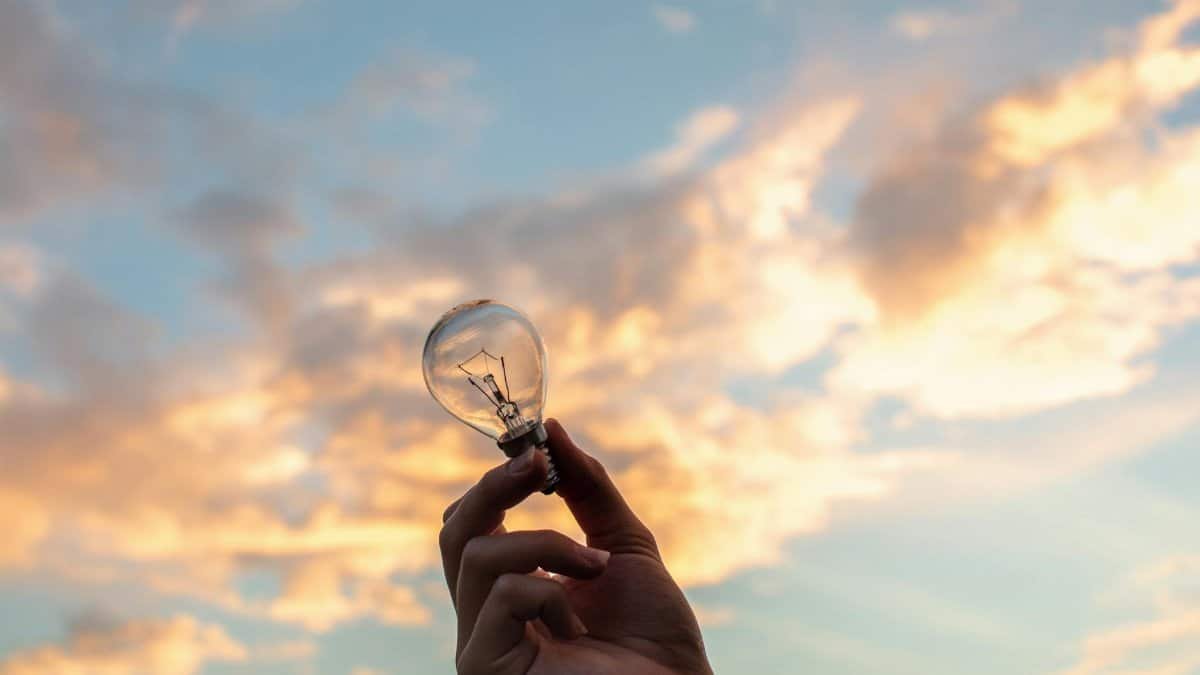 A hand holds a light bulb against a scenic sunset sky, symbolizing creativity and innovation.