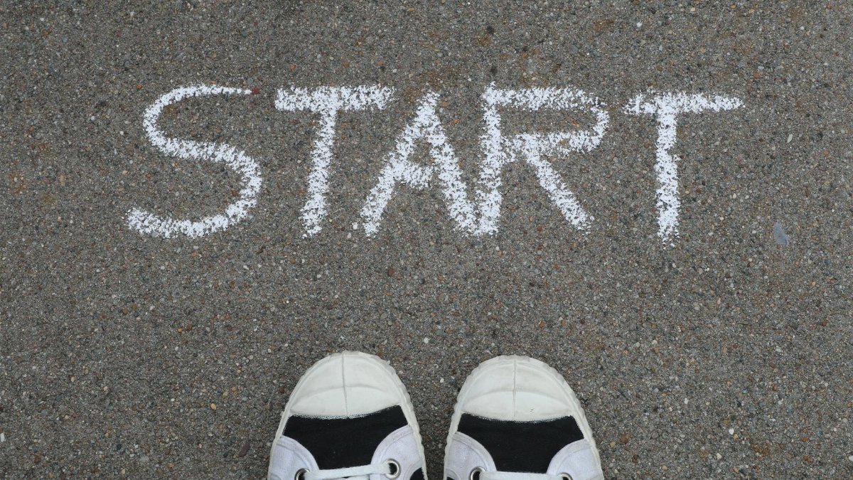Close-up of sneakers and a 'START' chalk drawing on pavement, symbolizing new beginnings.